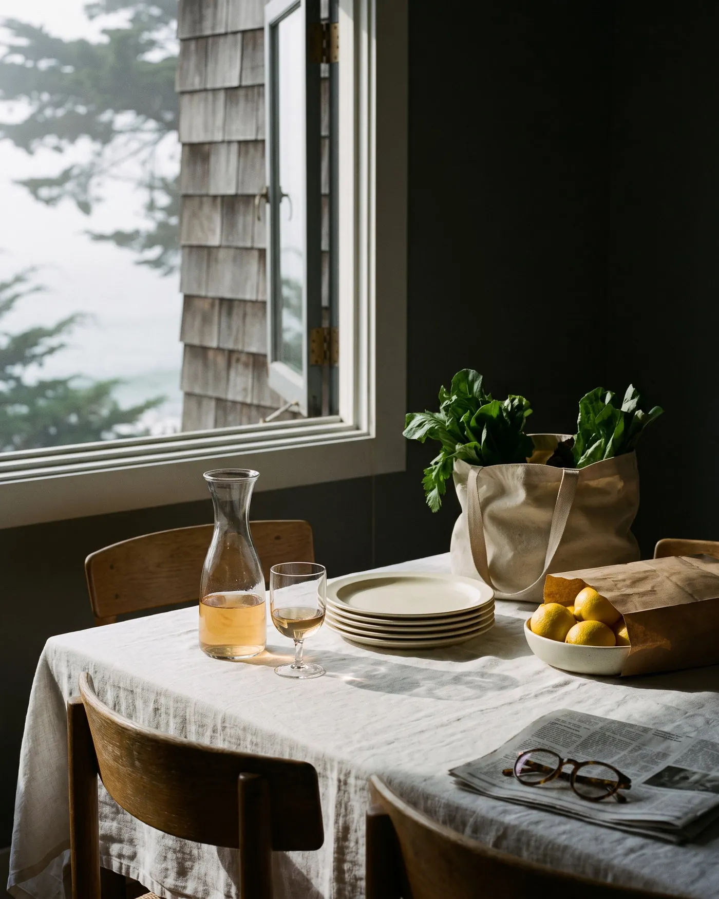 A Sunday table with linen, market greens and a carafe, beside an open coastal window.